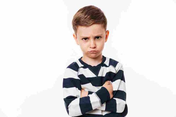 Child frowning with arms crossed against a white background